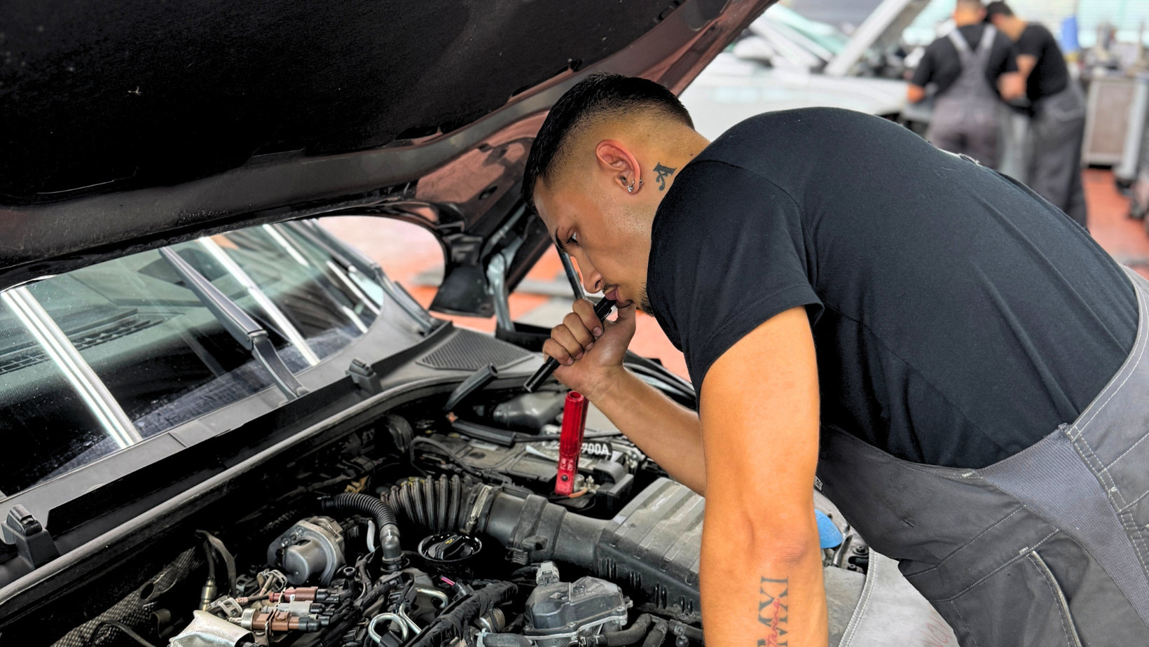 Werkstattmitarbeiter in einer Autowerkstatt, der den Motor eines Autos mit einer Taschenlampe untersucht
