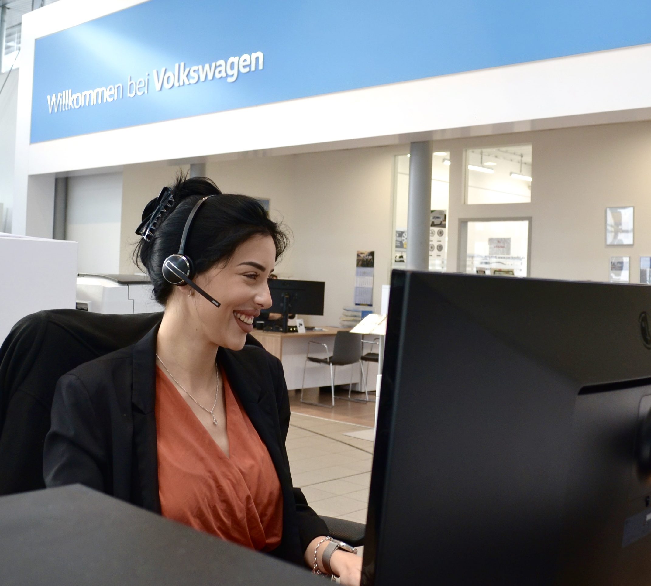 Servicemitarbeiterin am Empfang sitzt am Arbeitsplatz vor einem Bildschirm und hat ein Headset auf.